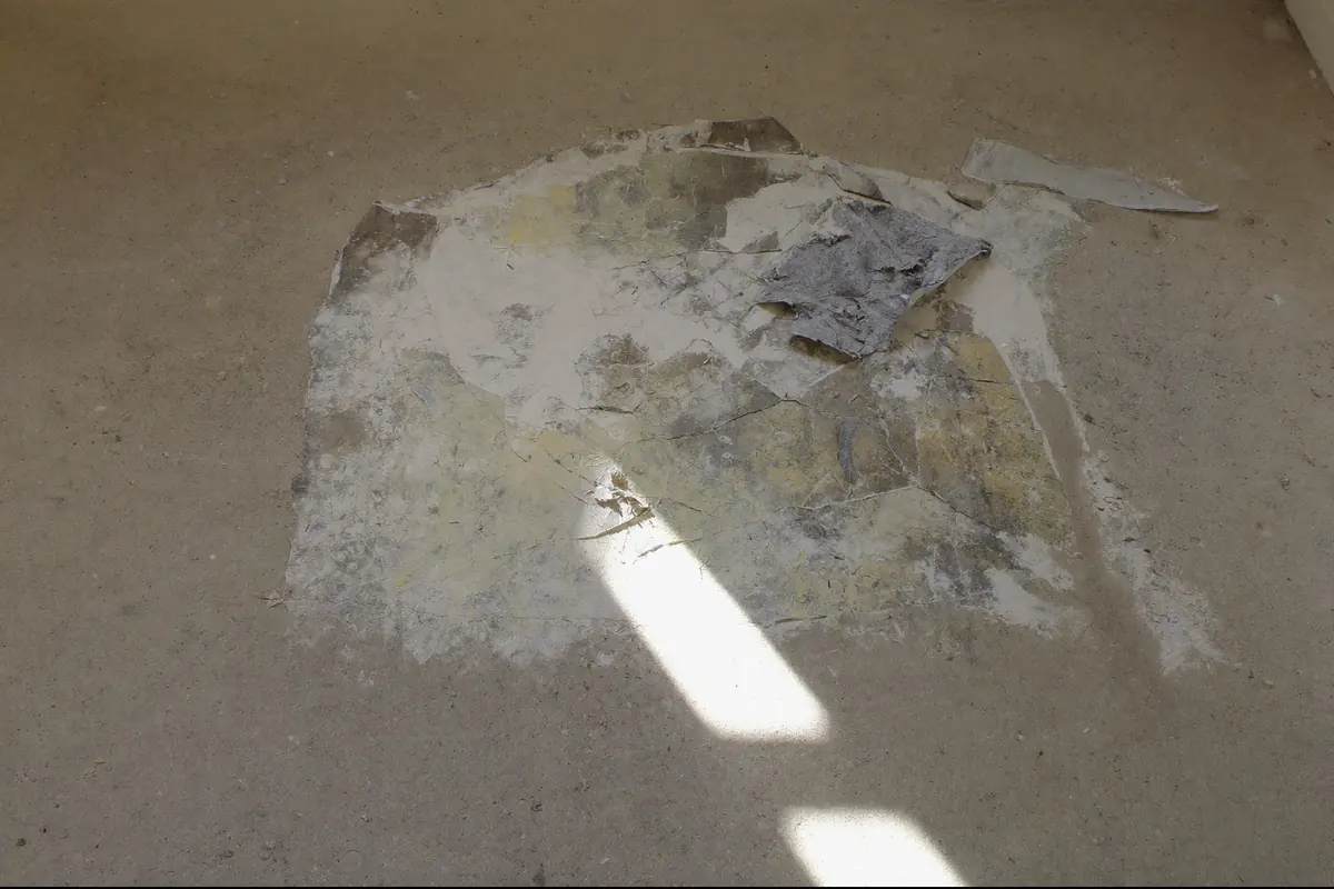 Betonvloer met een plek oude lijmresten en flarden grijze vinylrug na het verwijderen van een oude vloer